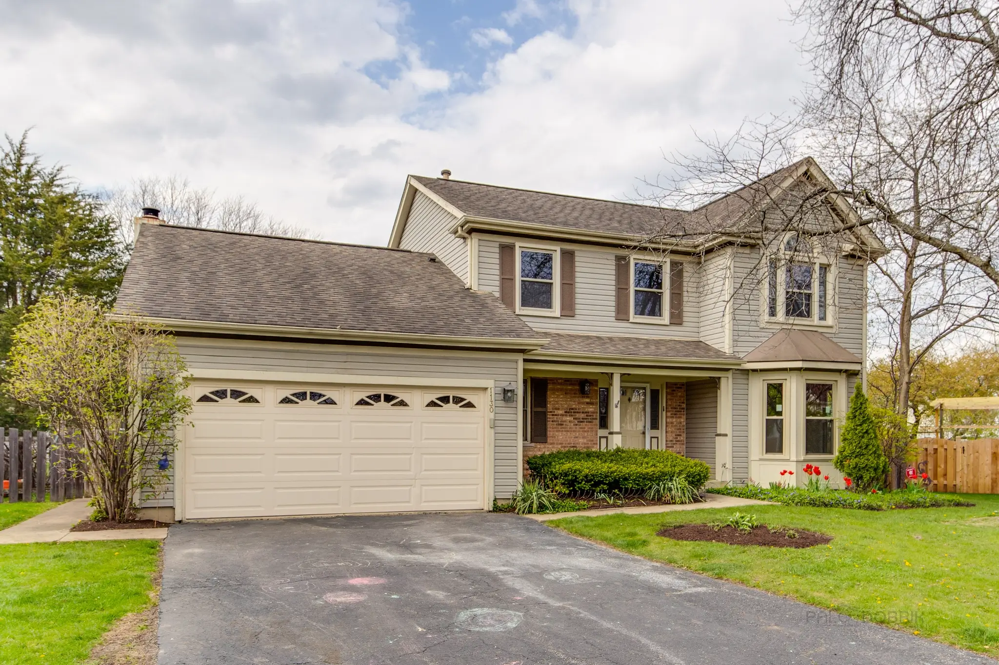 A two-story suburban house with beige siding, a double garage, and a well-kept front lawn