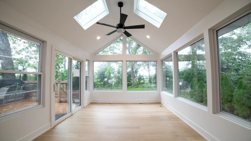 Bright sunroom with large windows and skylights, light wood flooring, and a ceiling fan