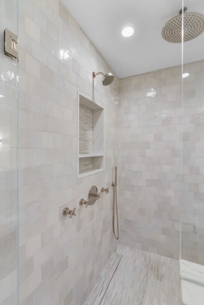 Modern shower with beige subway tiles, rain showerhead, handheld sprayer, and two niches