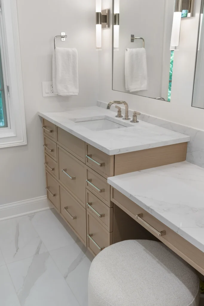 Modern bathroom with light wood cabinetry, white marble countertops, and silver fixtures