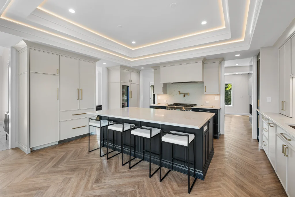 Modern kitchen with white cabinetry, black island with four stools, herringbone wood floor, and recessed ceiling lighting, creating a sleek, inviting space