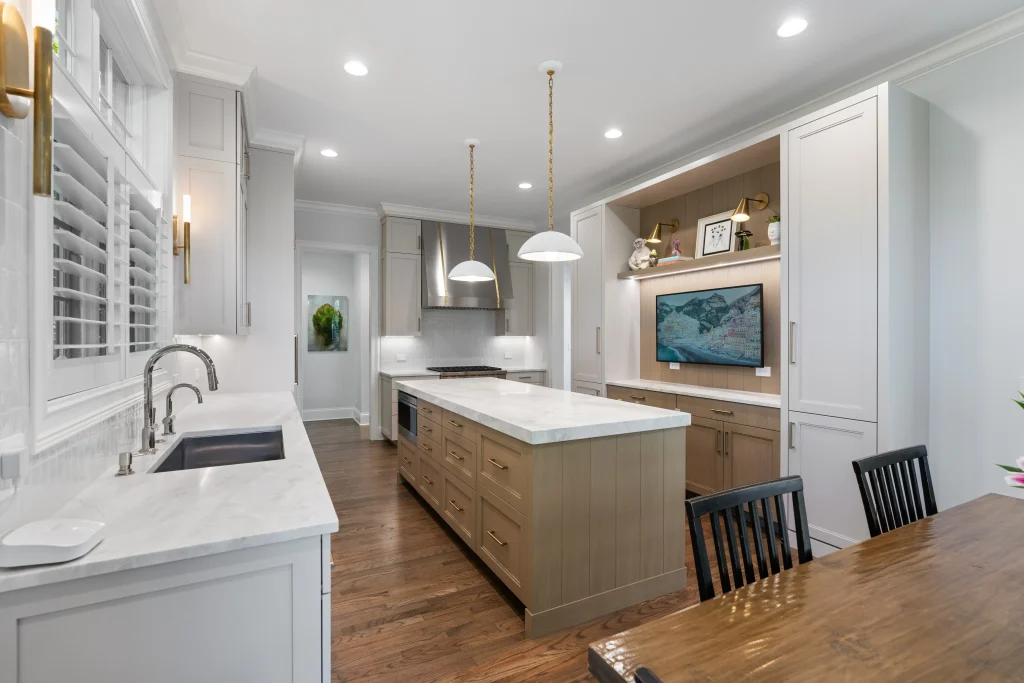 A modern kitchen with white cabinets, a marble island, pendant lights, and wooden flooring