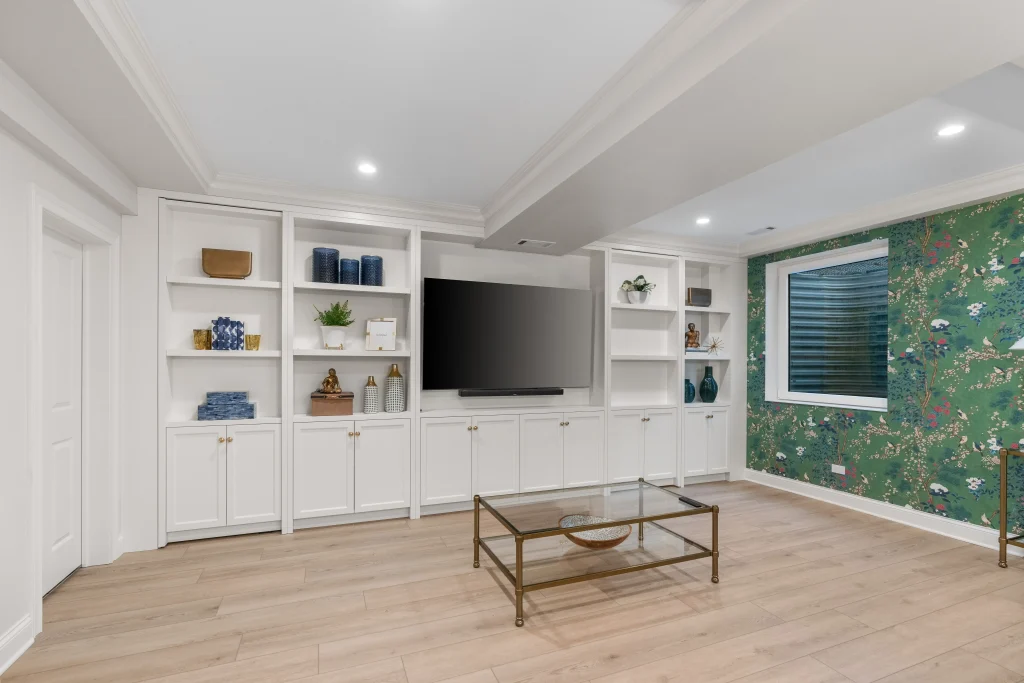 Stylish living room with built-in white shelves, a large TV, decorative items, and floral wallpaper