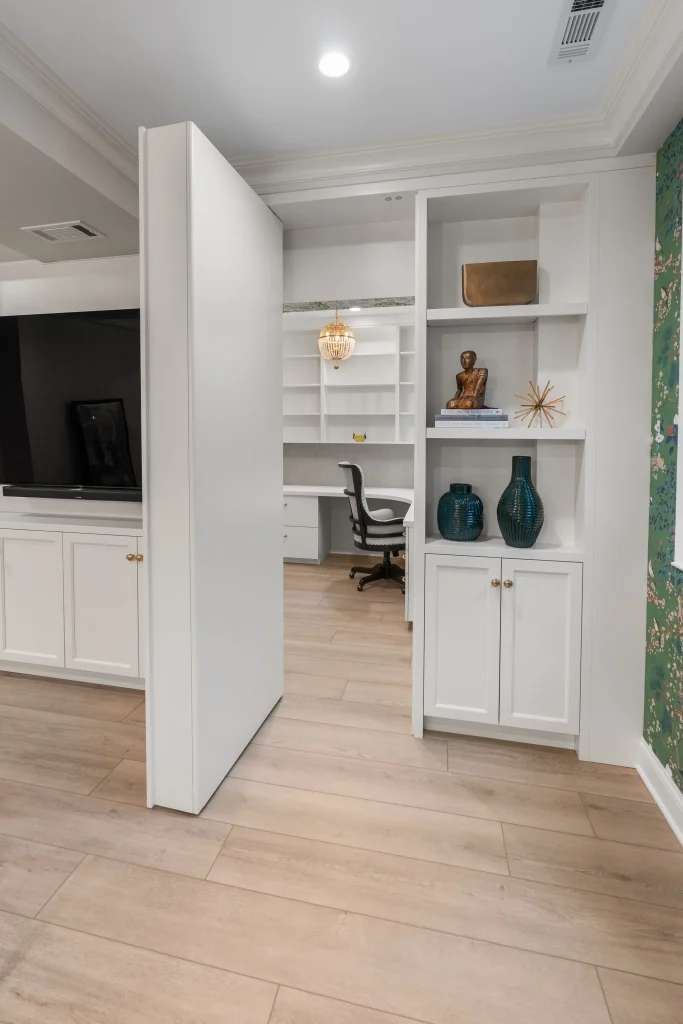 Hidden office behind a swivel bookcase with sleek white shelves, blue vases, and a wooden statue