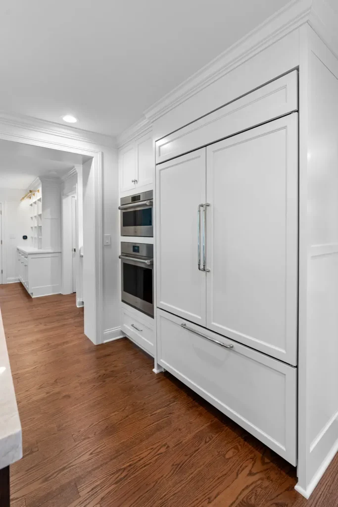 A sleek, modern kitchen featuring white cabinetry and stainless steel appliances, including a built-in oven and fridge