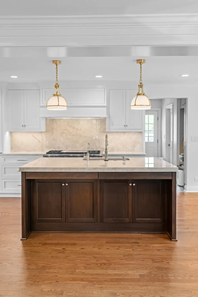 A bright kitchen with a central dark wood island, pendant lights, and white cabinets