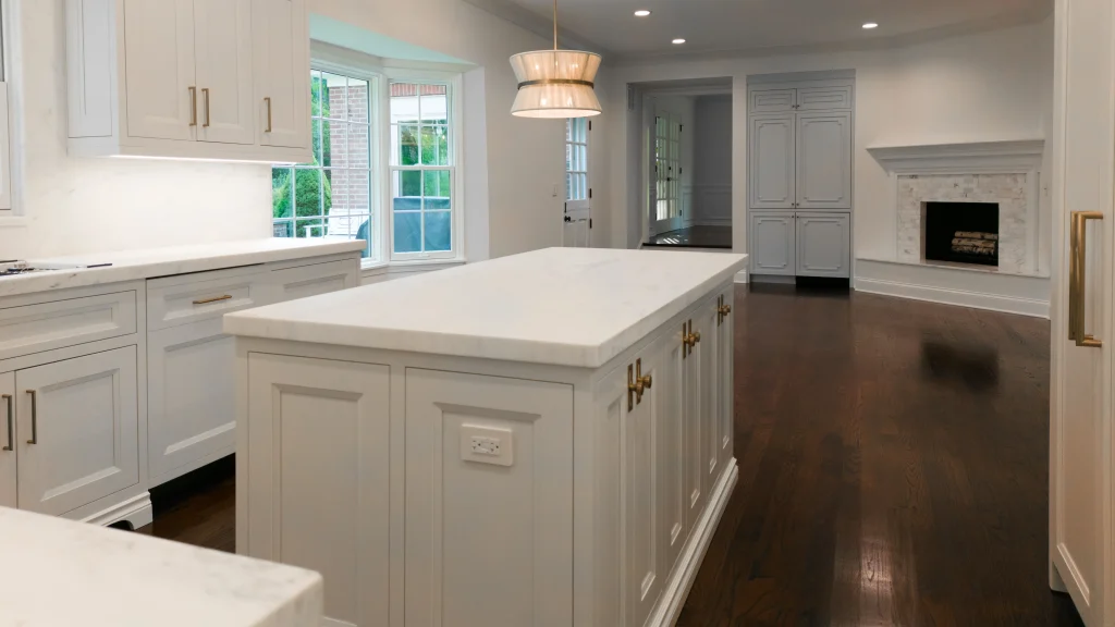 Spacious kitchen with a large white marble island, white cabinets, and dark wooden floors