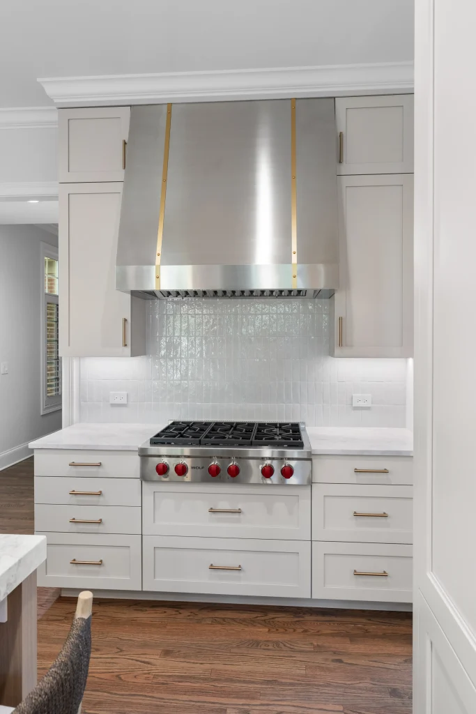 A modern kitchen features a stainless steel stove with red knobs and a large range hood