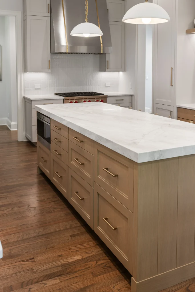 Modern kitchen with a large wooden island featuring a marble countertop and brass handles