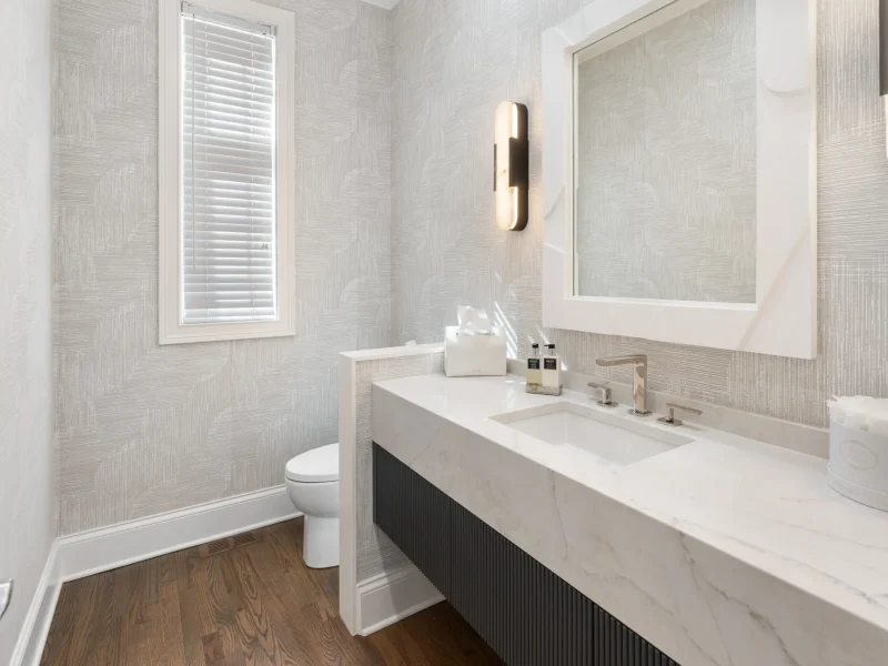 A modern bathroom with white marble sink, large mirror, wooden floor, and textured gray wallpaper