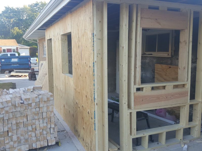 A partially constructed wooden extension on a house, with exposed plywood and lumber