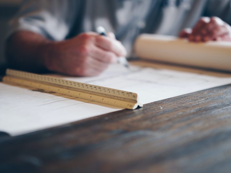 A person is sketching on rolled out architectural plans with a pen