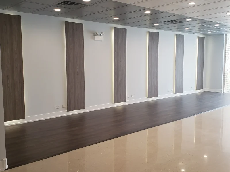 A spacious, modern room with a polished reflective floor, dark wooden accent panels on white walls