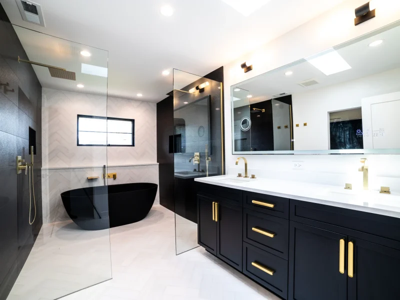 Modern bathroom with black and gold accents. Features a black bathtub, glass shower, and double vanity with large mirror