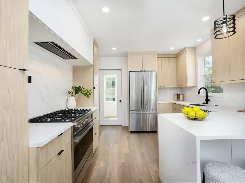 Modern kitchen with light wood cabinets, white marble countertops, and stainless steel appliances