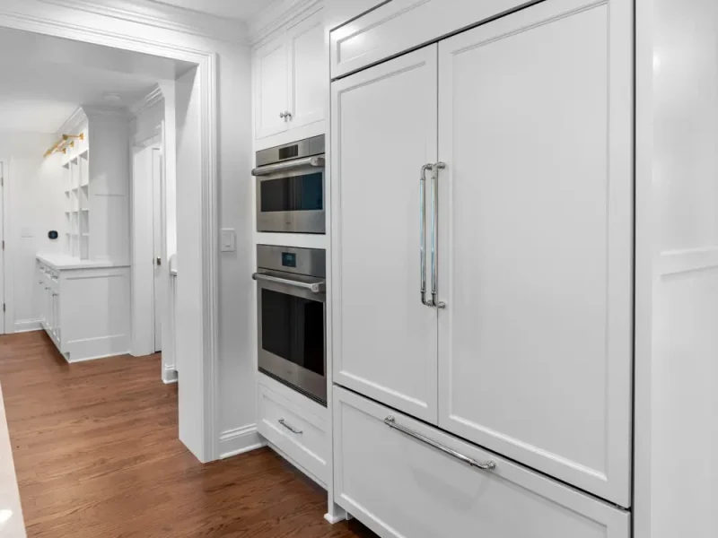 A sleek, modern kitchen featuring white cabinetry and stainless steel appliances, including a built-in oven and fridge