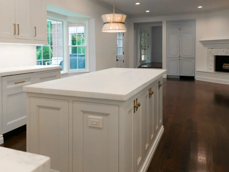 Spacious kitchen with a large white marble island, white cabinets, and dark wooden floors