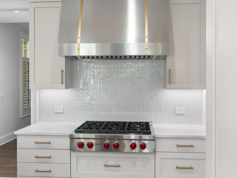 A modern kitchen features a stainless steel stove with red knobs and a large range hood
